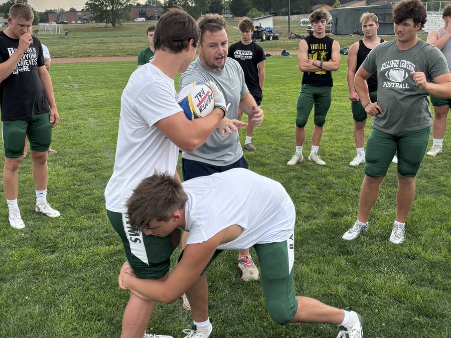 Coach demonstrating a rugby-style tackle wrap with Billings Central players